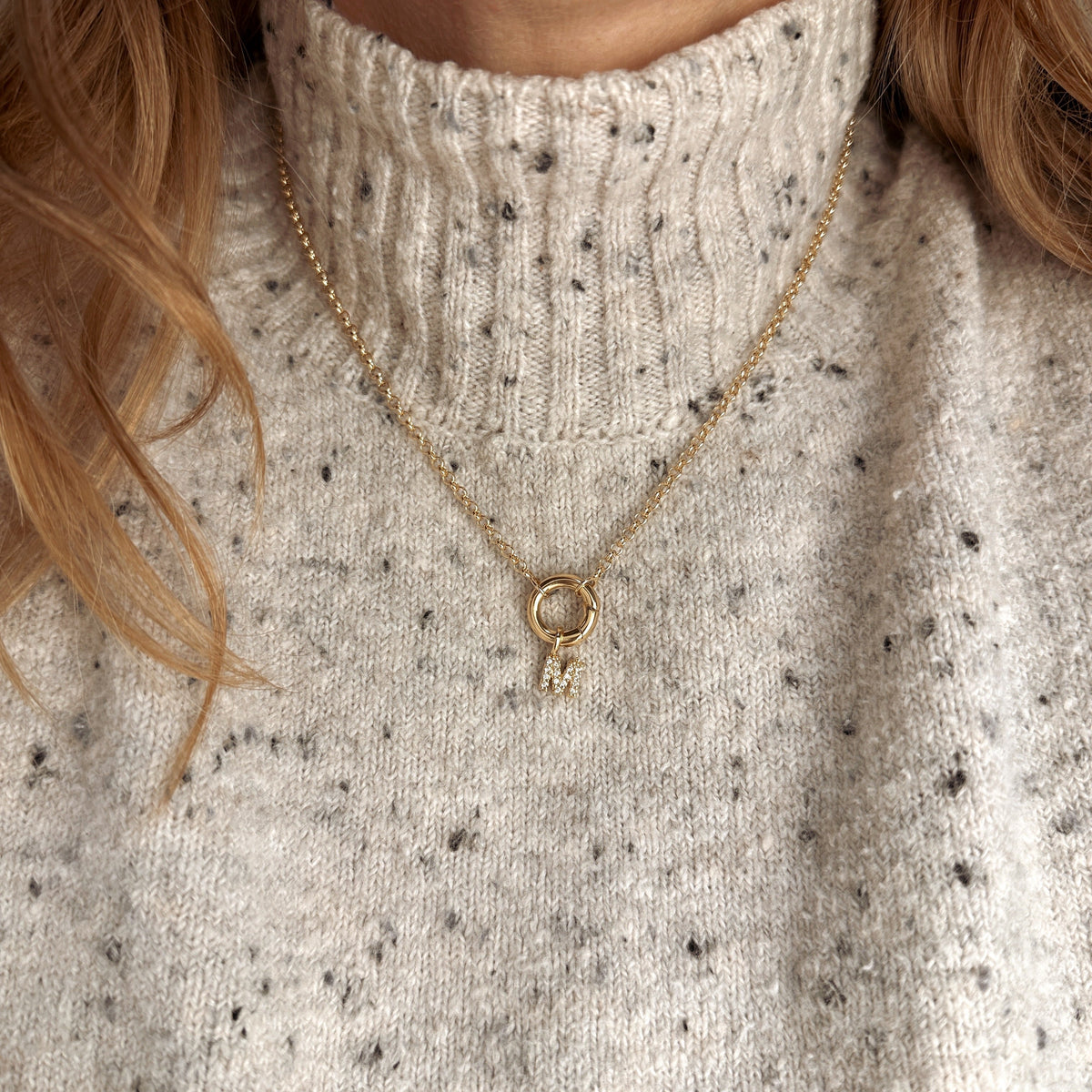Woman wearing a pavé CZ initial charm necklace in 18K gold-filled over a speckled knit sweater