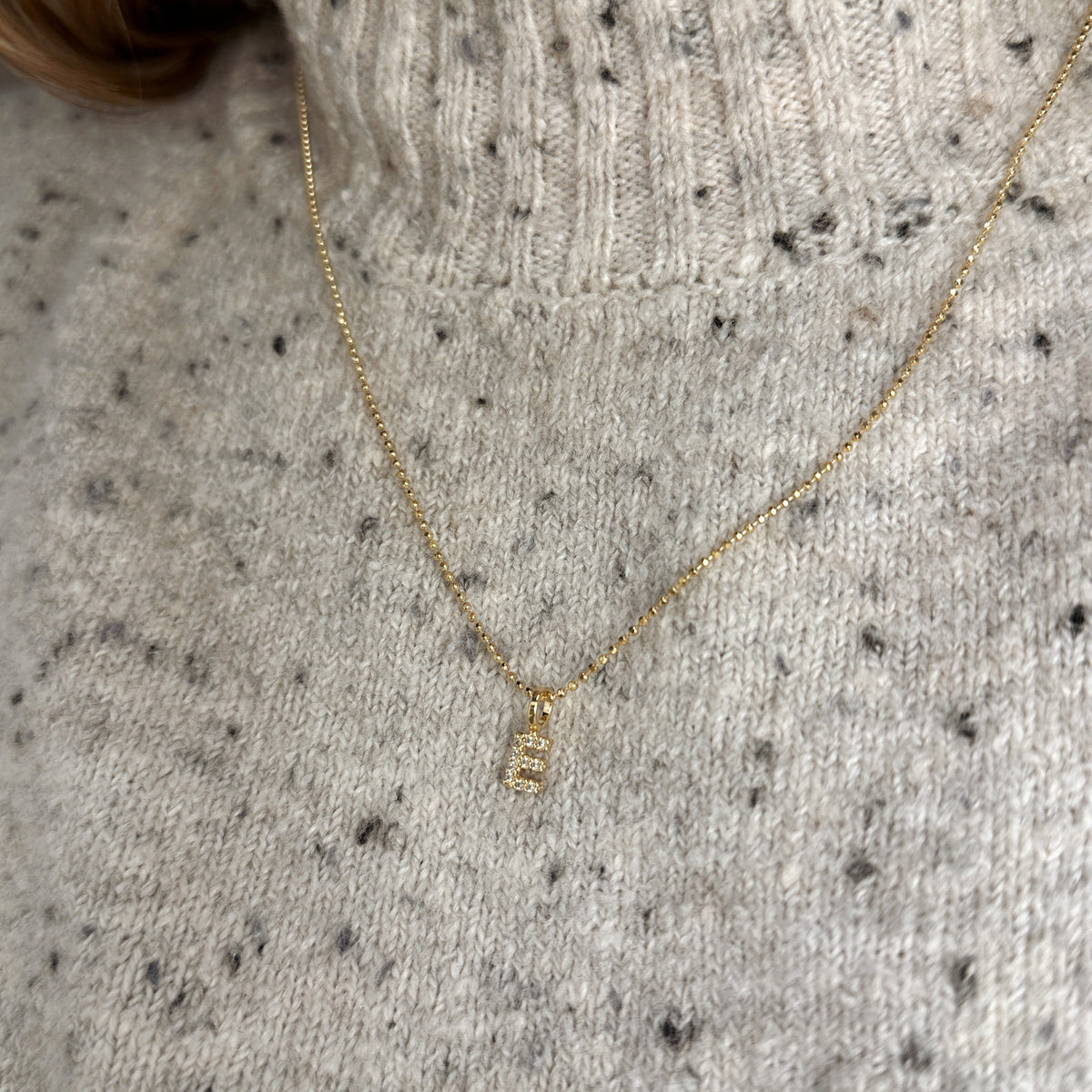 Pavé CZ initial charm on a dainty 18K gold-filled chain worn over a knit sweater