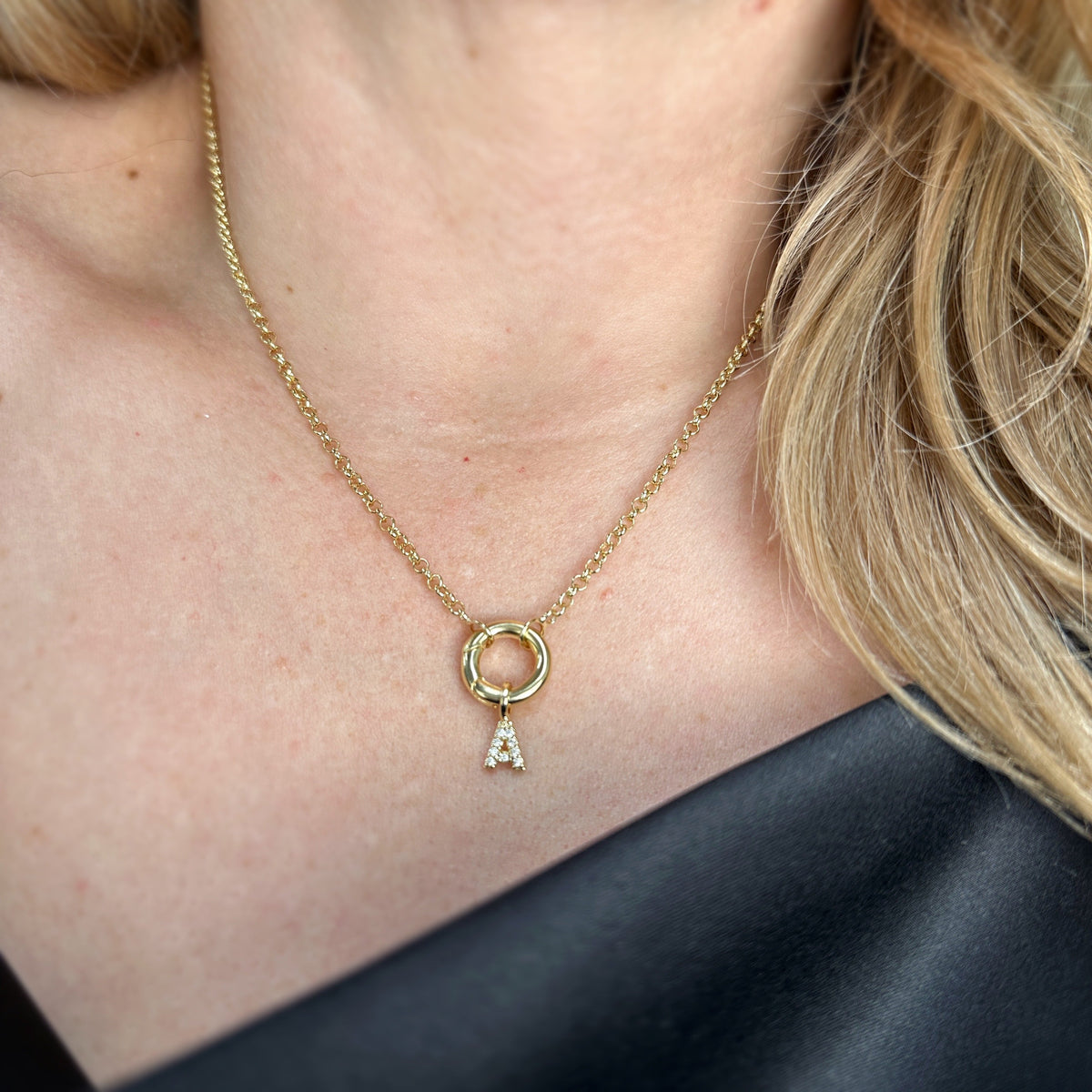 Close-up of a letter A pavé CZ initial charm necklace in 18K gold-filled worn with a black top