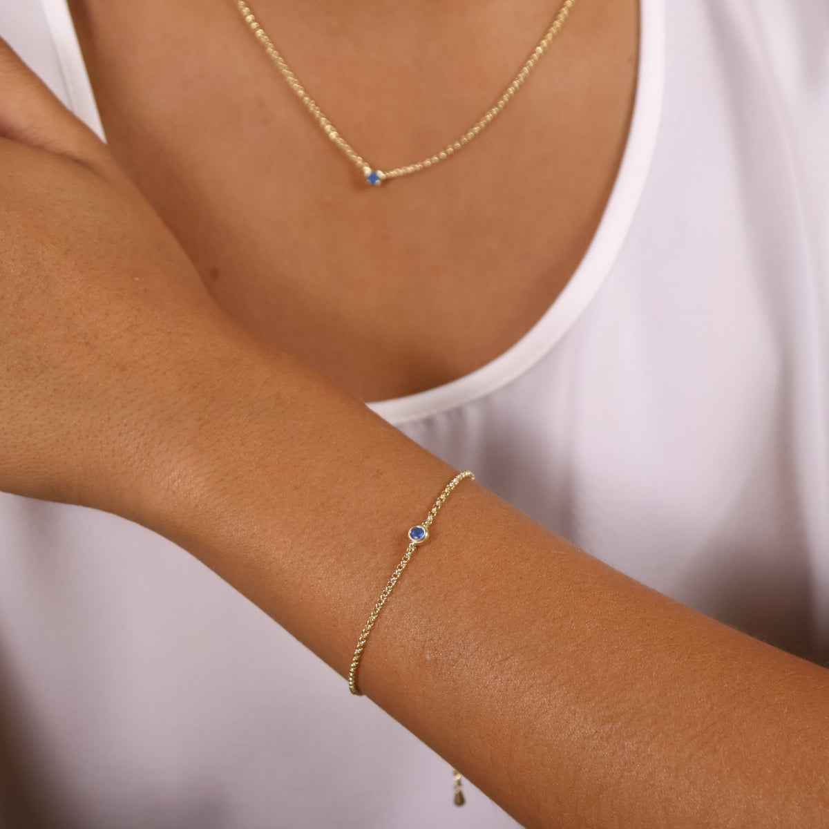 Close-up of a woman's wrist wearing an 18k gold filled dainty bezel CZ birthstone bracelet with a blue stone.