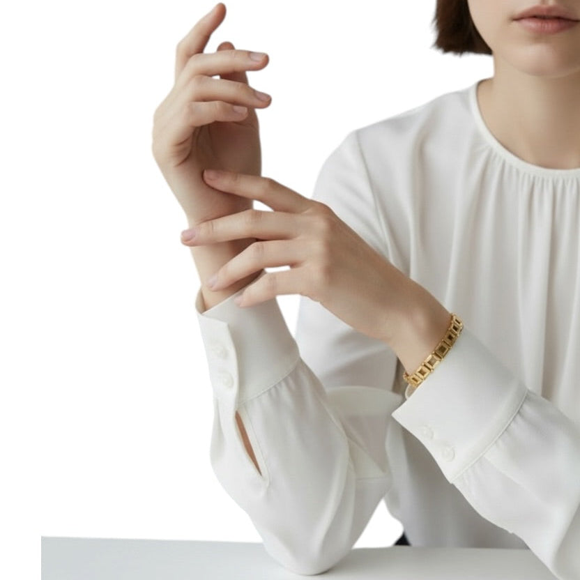 Person wearing a white shirt with a gold bracelet on a plain background