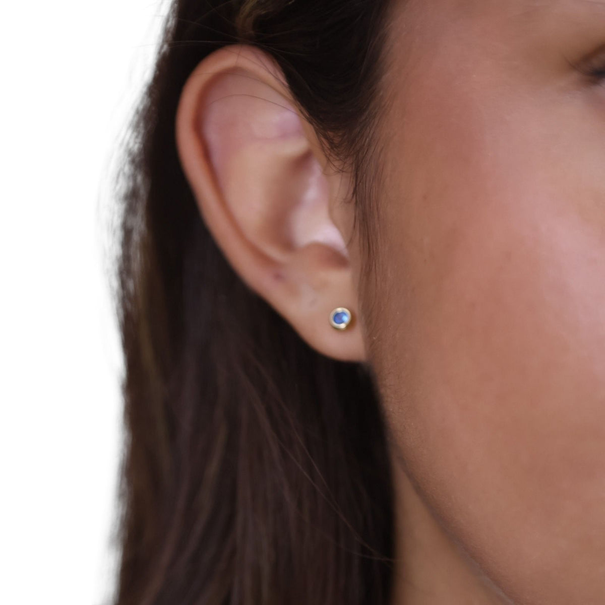 Close-up of a light blue birthstone bezel stud earring in 18K gold-filled worn on the ear