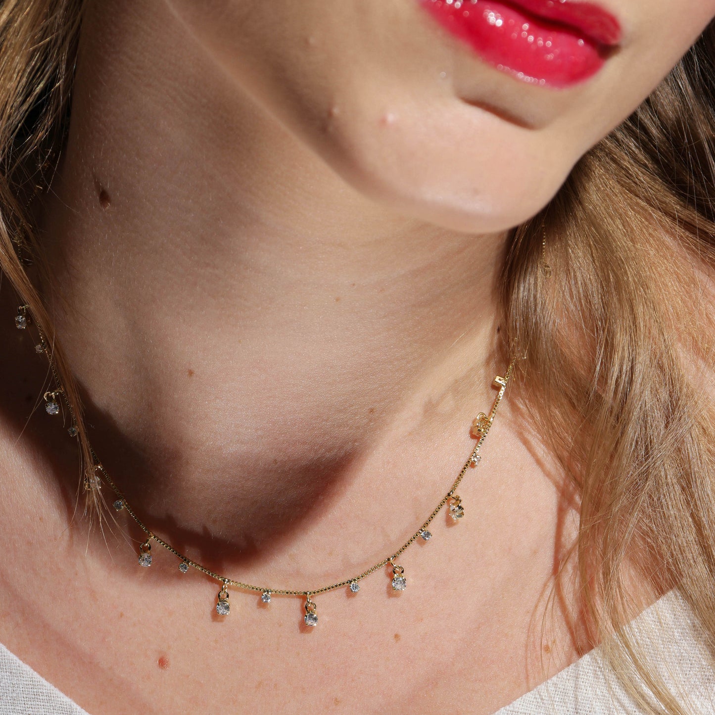 Close-up of a woman wearing a delicate gold necklace with small stones.