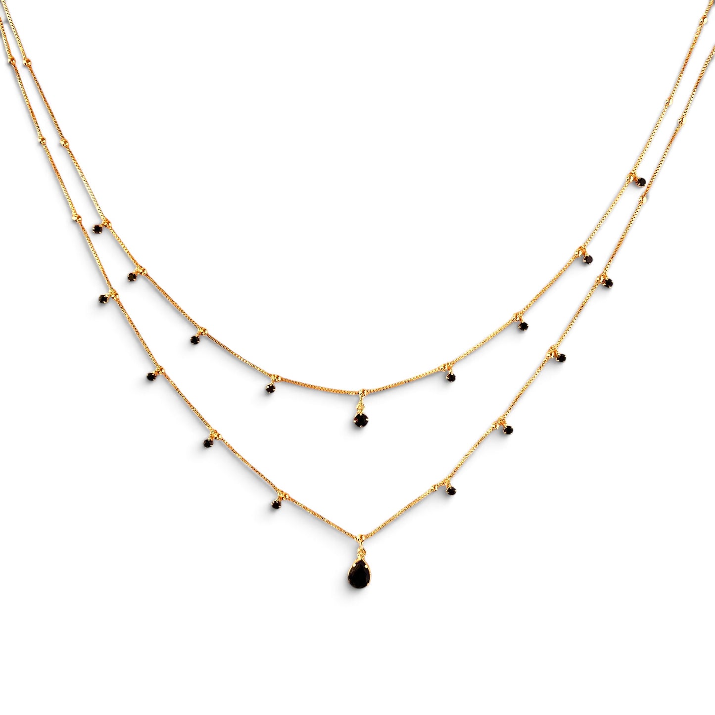 A double-layered gold necklace with small black bead accents and a teardrop-shaped black pendant