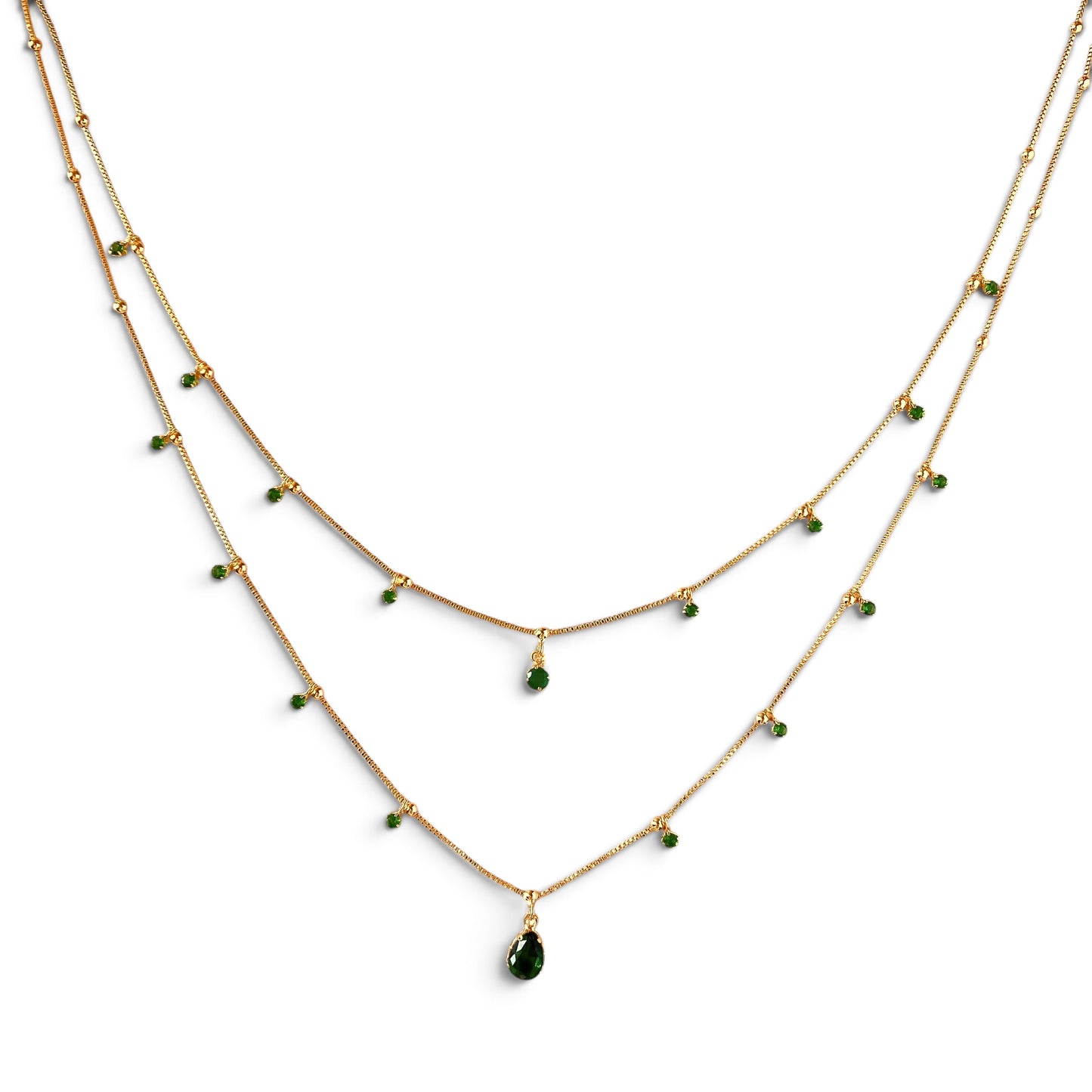 A double-layered gold necklace with small green bead accents and a teardrop-shaped green gemstone pendant, displayed on a clean white background.