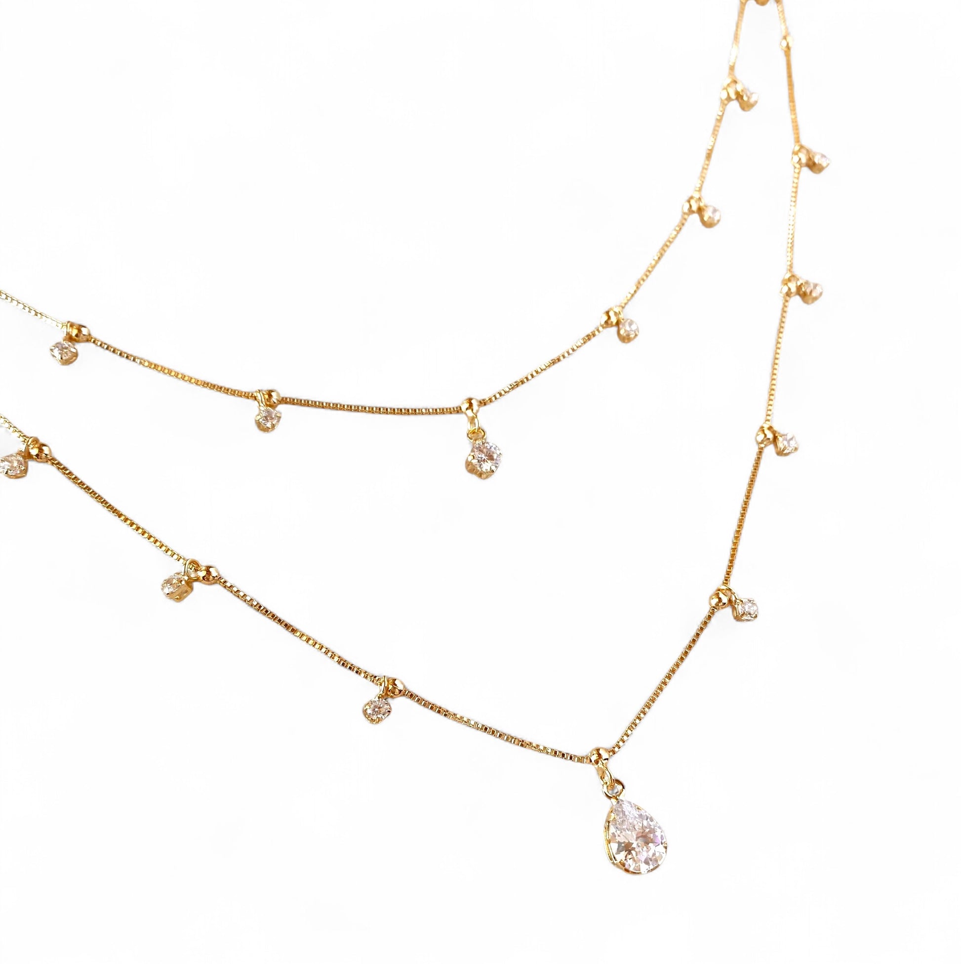 A gold-toned double-layer necklace featuring a teardrop-shaped clear crystal pendant