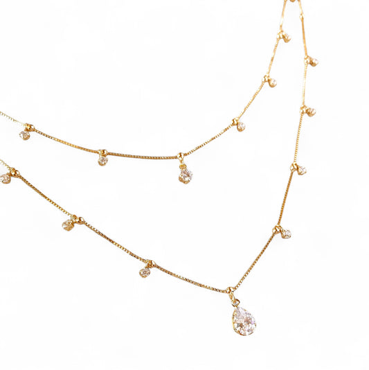 A gold-toned double-layer necklace featuring a teardrop-shaped clear crystal pendant