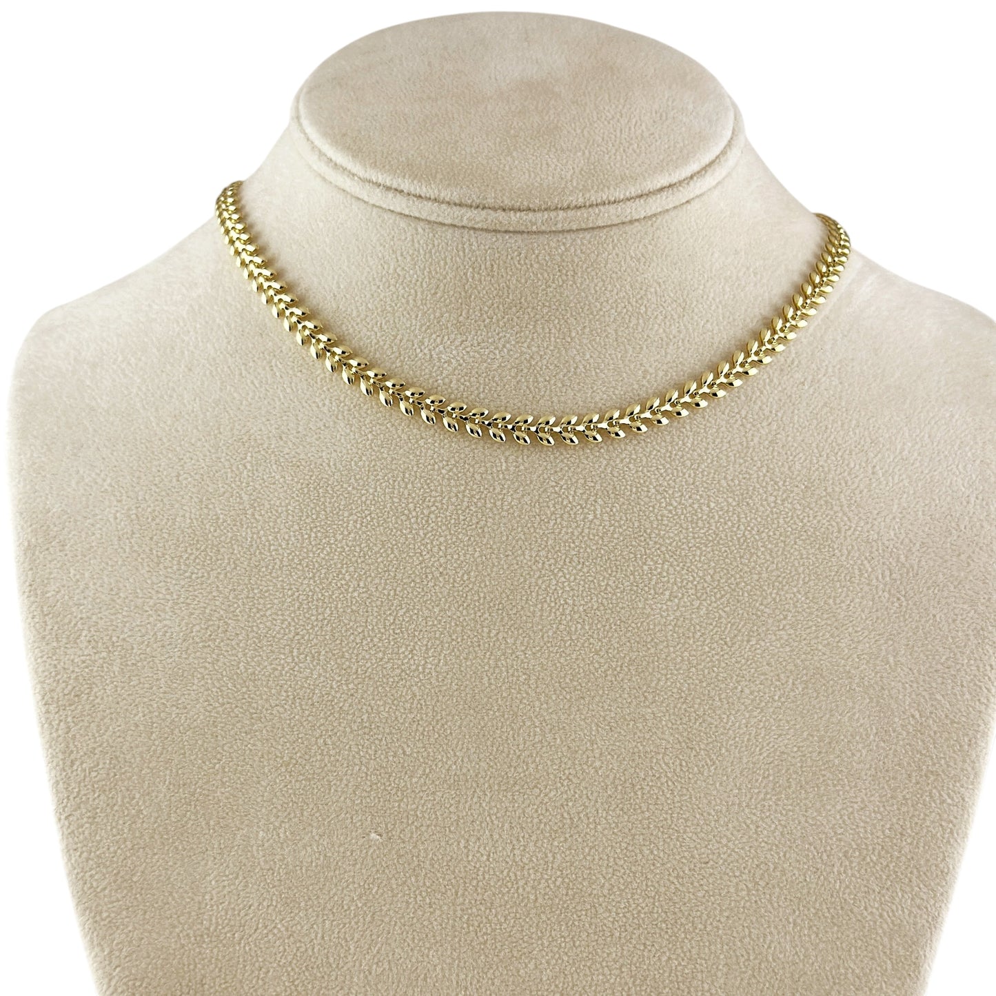 A gold chain necklace displayed on a beige fabric jewelry bust against a white background.