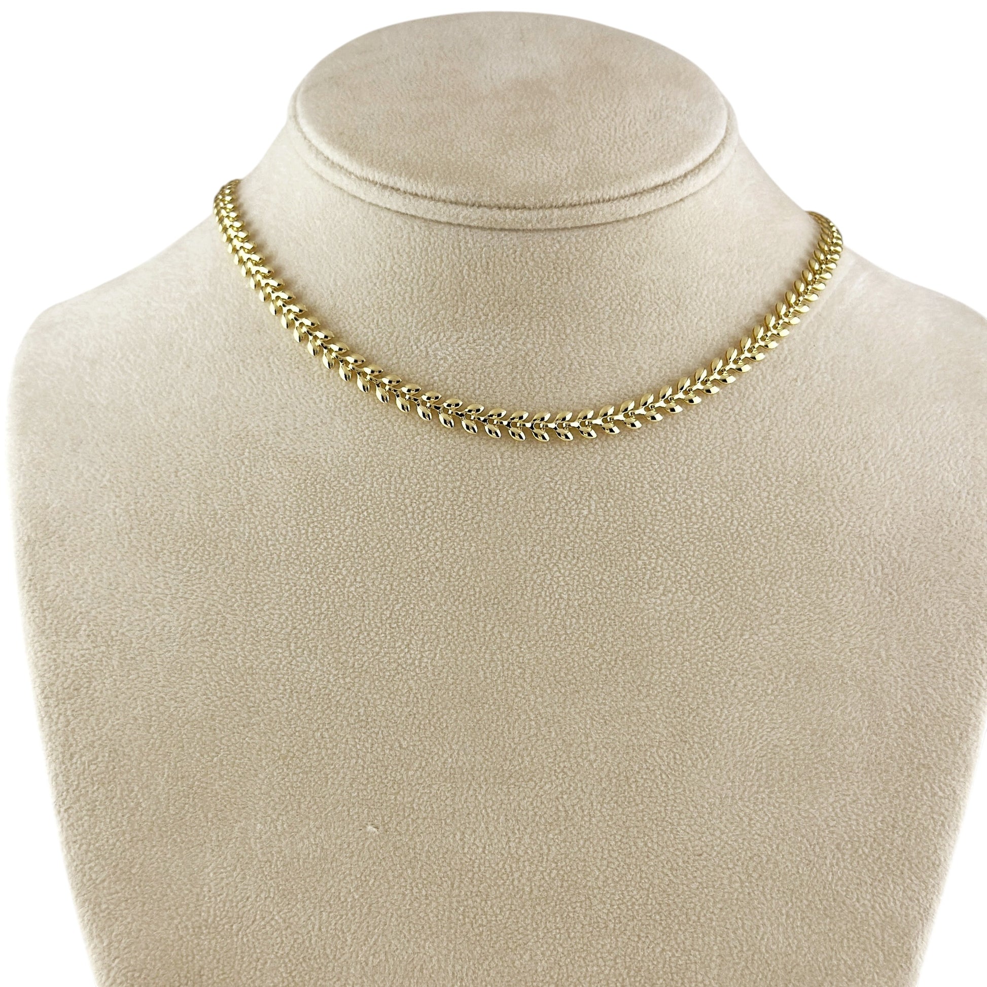 A gold chain necklace displayed on a beige fabric jewelry bust against a white background.