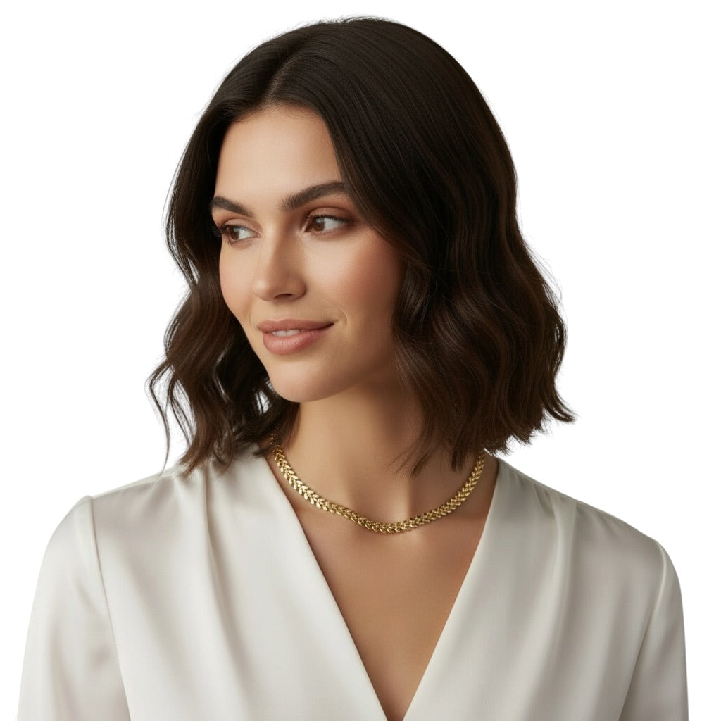 A woman with dark brown shoulder-length wavy hair wearing a gold chain necklace