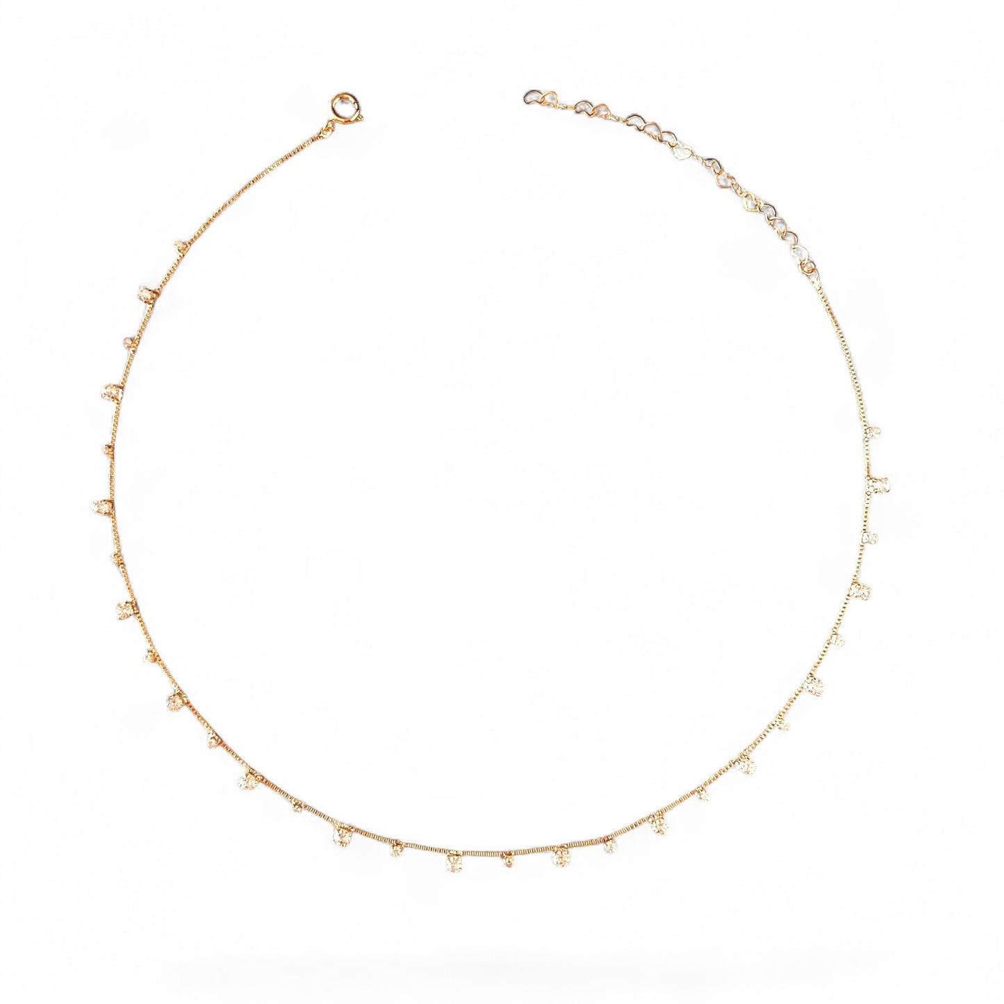 A delicate gold chain necklace with small, evenly spaced clear crystal beads, displayed in a circular shape against a solid white background.