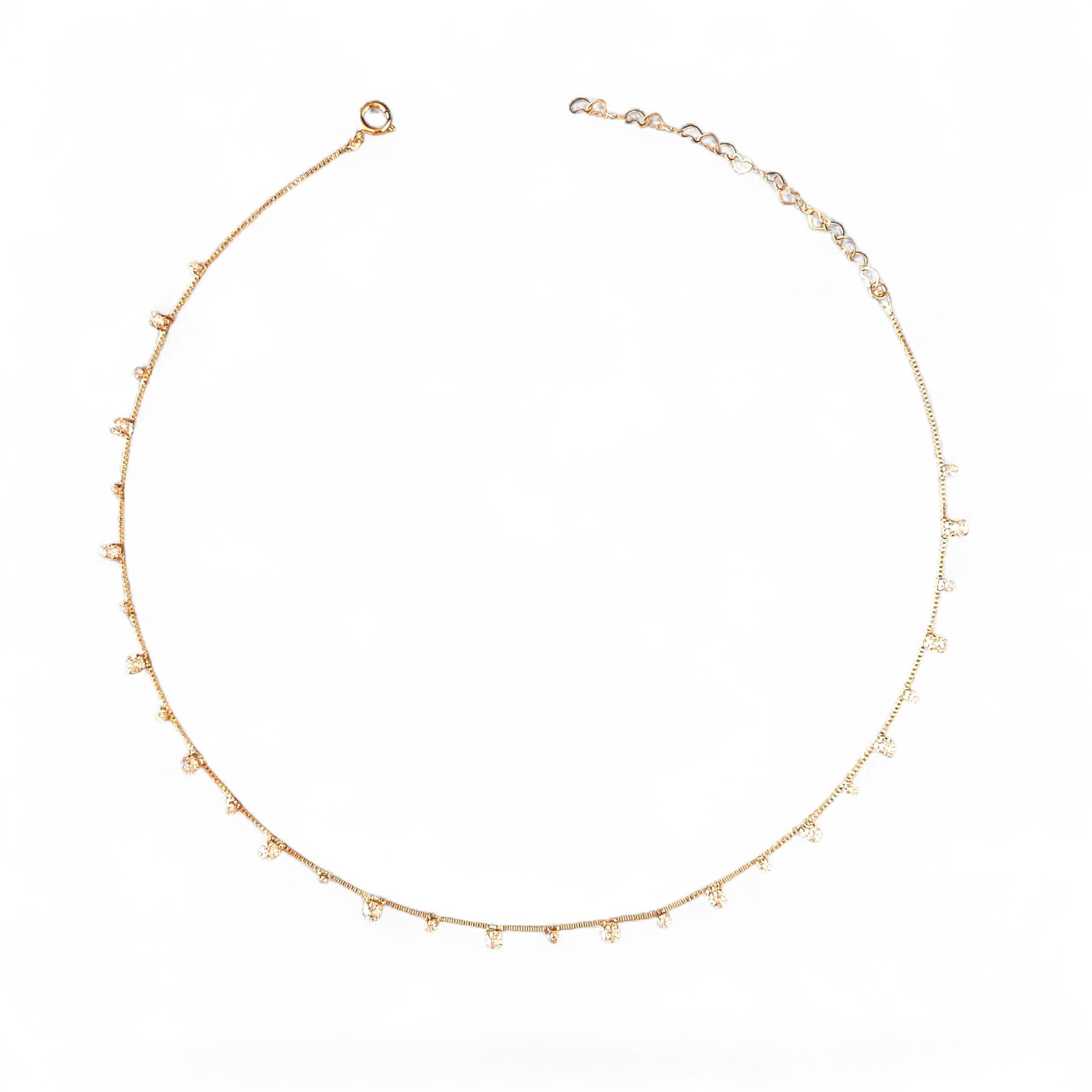 A delicate gold chain necklace with small, evenly spaced clear crystal beads, displayed in a circular shape against a solid white background.