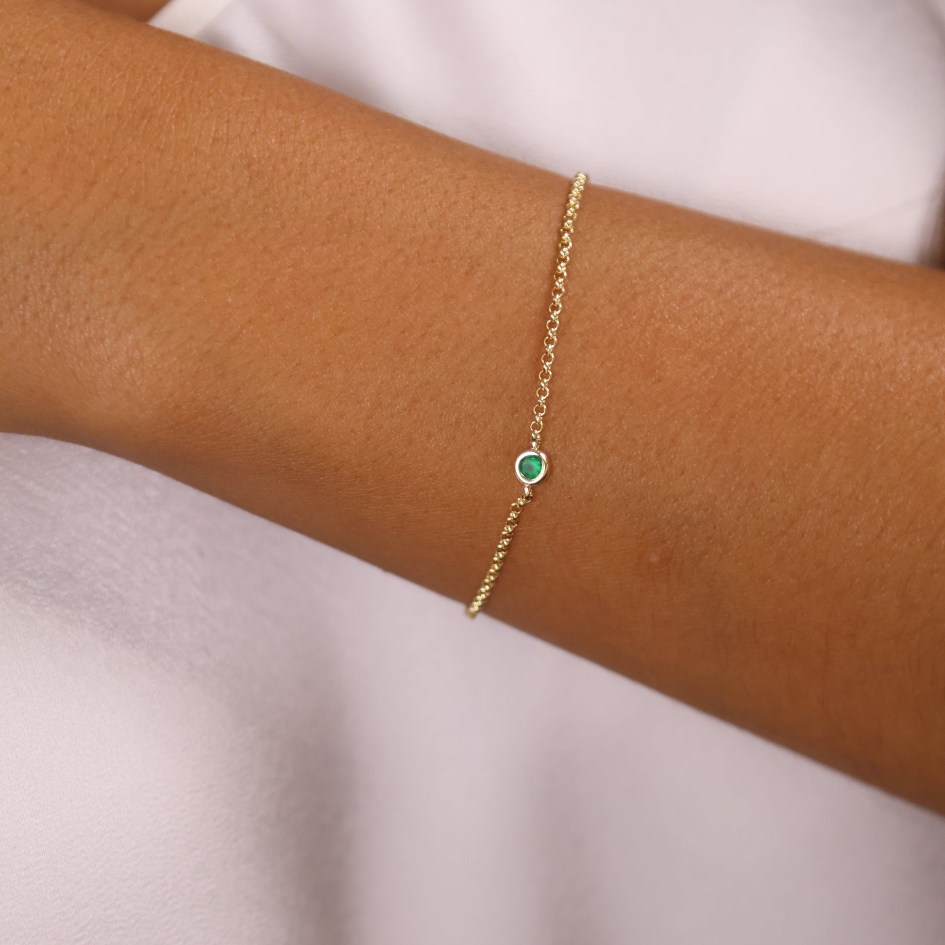 Dainty 18K gold filled bracelet on wrist featuring a bezel-set green cubic zirconia birthstone, elegant and delicate design.