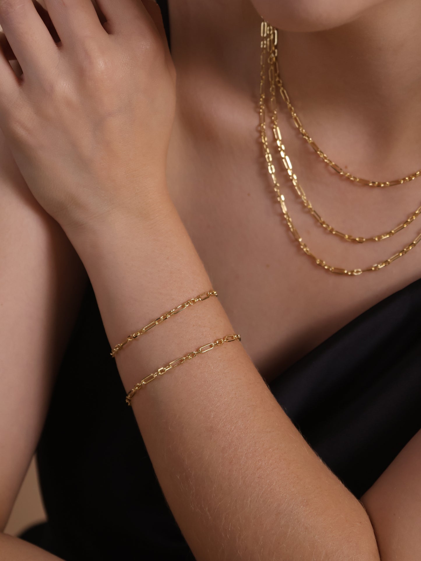 Close-up of a model wearing an 18K gold filled alternated paperclip bracelet and layered necklaces, showcasing contemporary style.