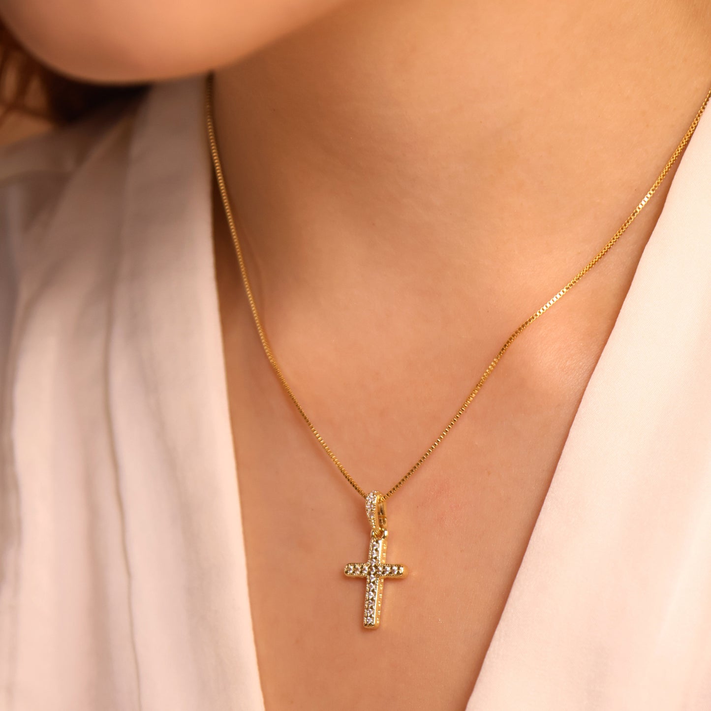 Gold necklace with a cross pendant on a person wearing a light pink top.