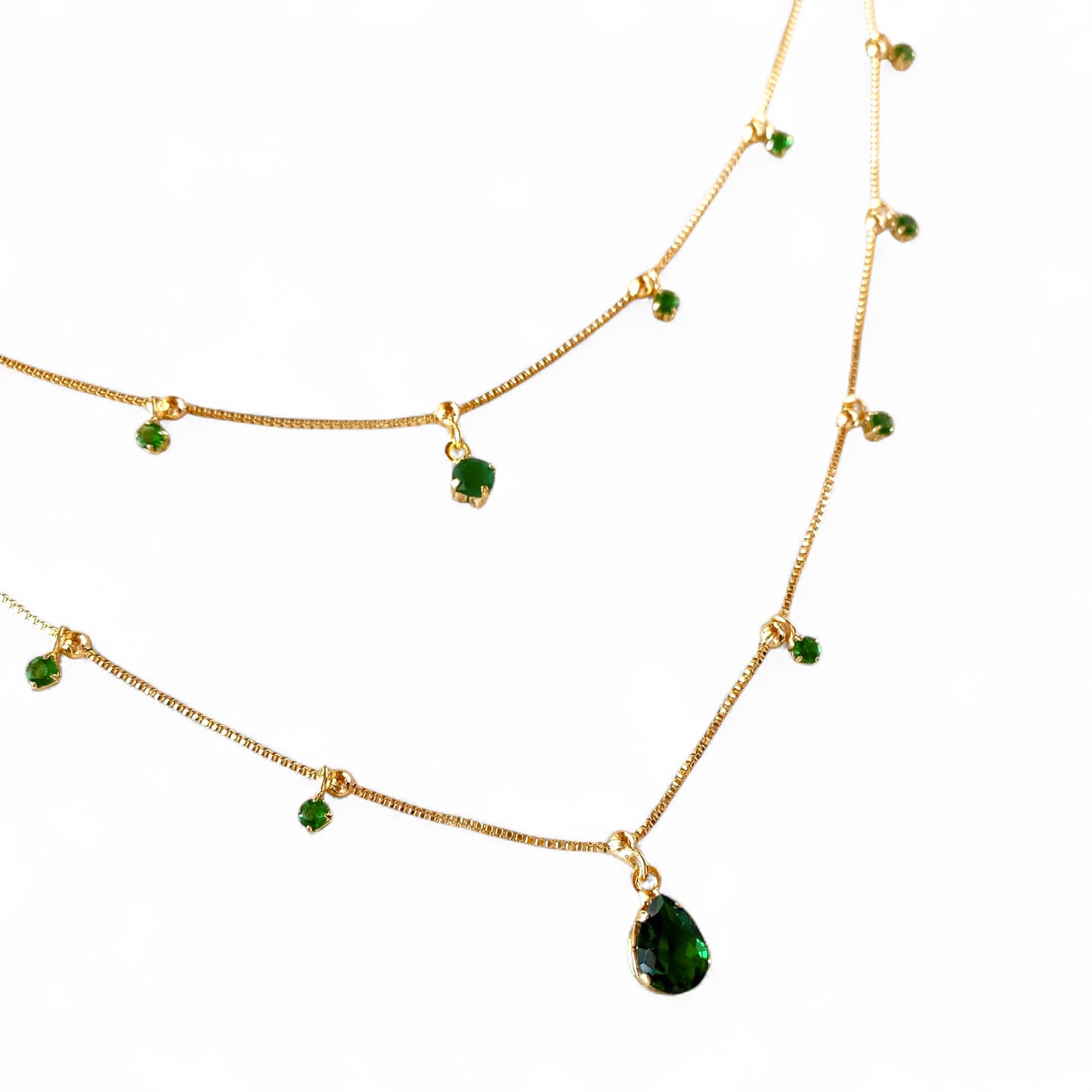 A gold-toned layered necklace set featuring a main chain with a teardrop-shaped green gemstone pendant and two thinner chains adorned with small round green gemstones, shown on a plain white background.